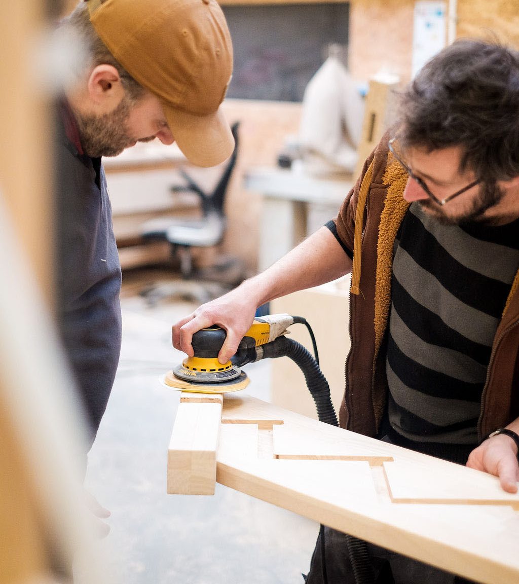 L'atelier en activité — menuisiers au travail sur une pièce